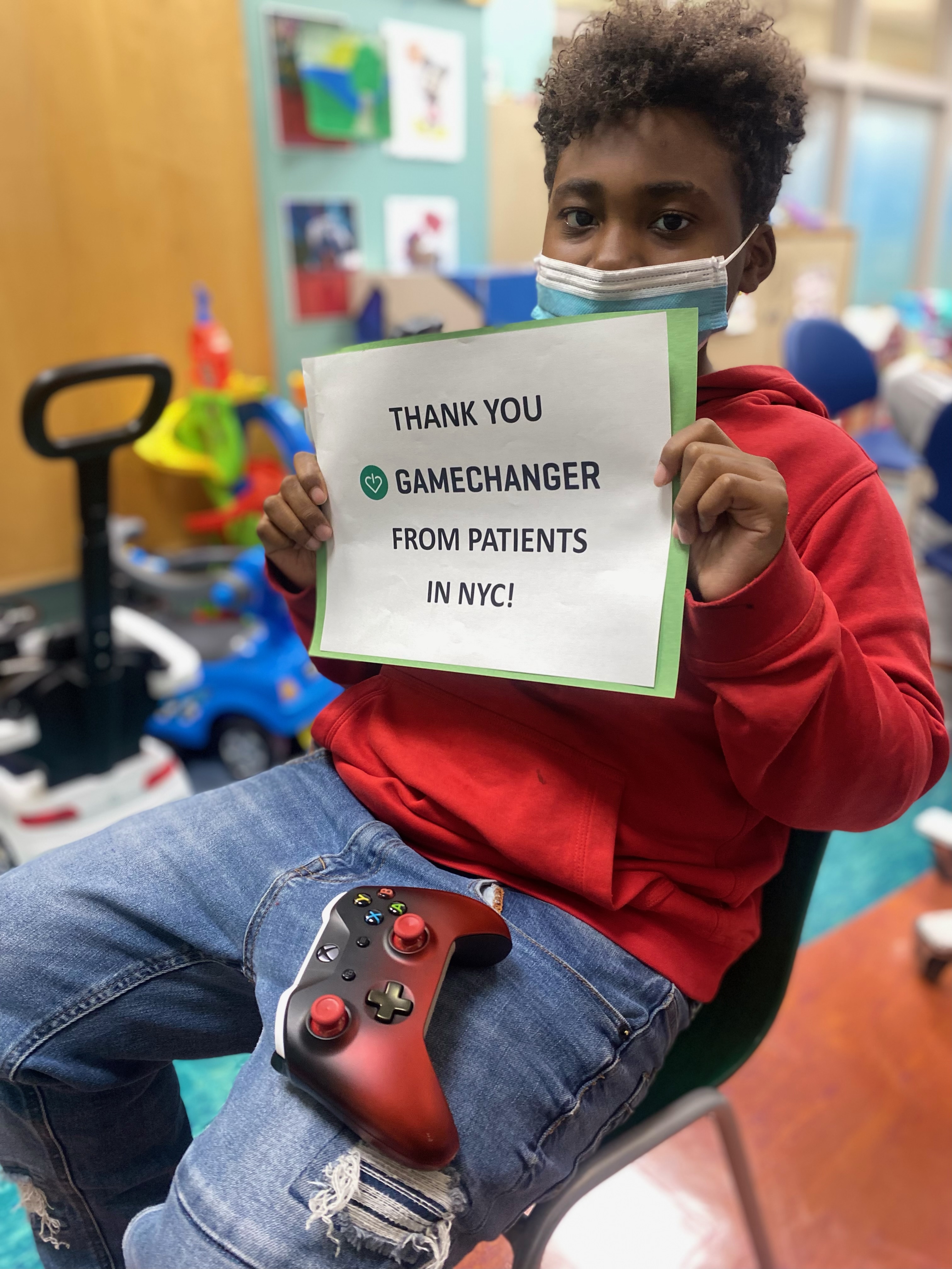 A young patient in a hospital playroom holding a hand-made &lsquo;Thank you, GameChanger&rsquo; sign.